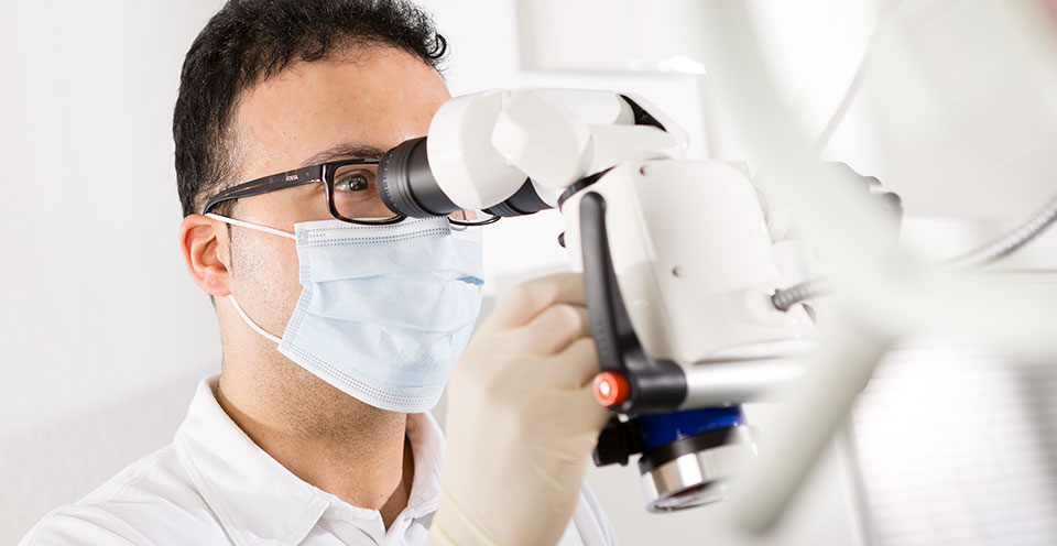 Ein Zahnarzt arbeitet konzentriert mit Mikroskop in moderner Zahnarztpraxis.